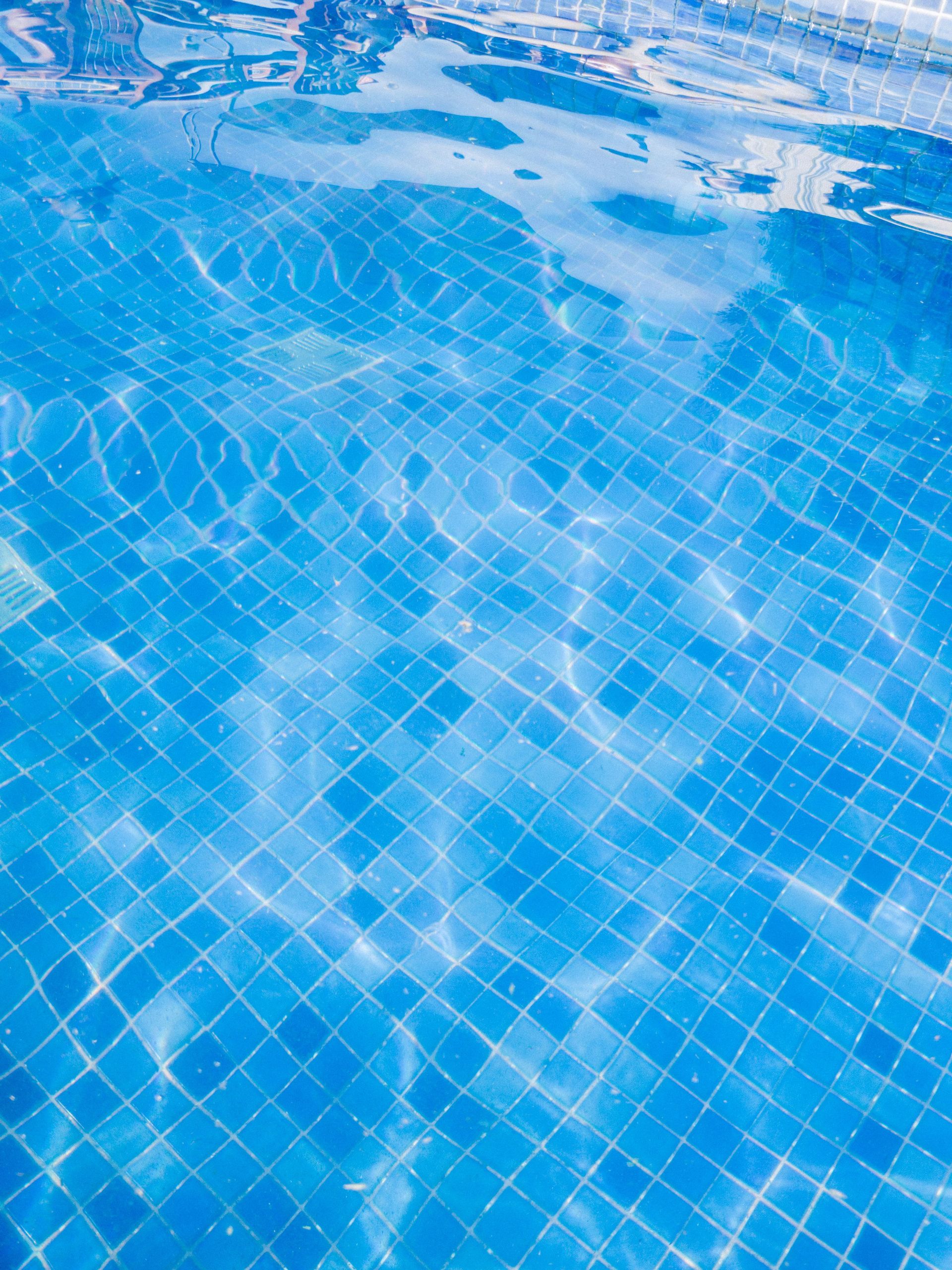 Close-up of vibrant blue pool tiles under clear water, reflecting sunlight for a refreshing summertime vibe.