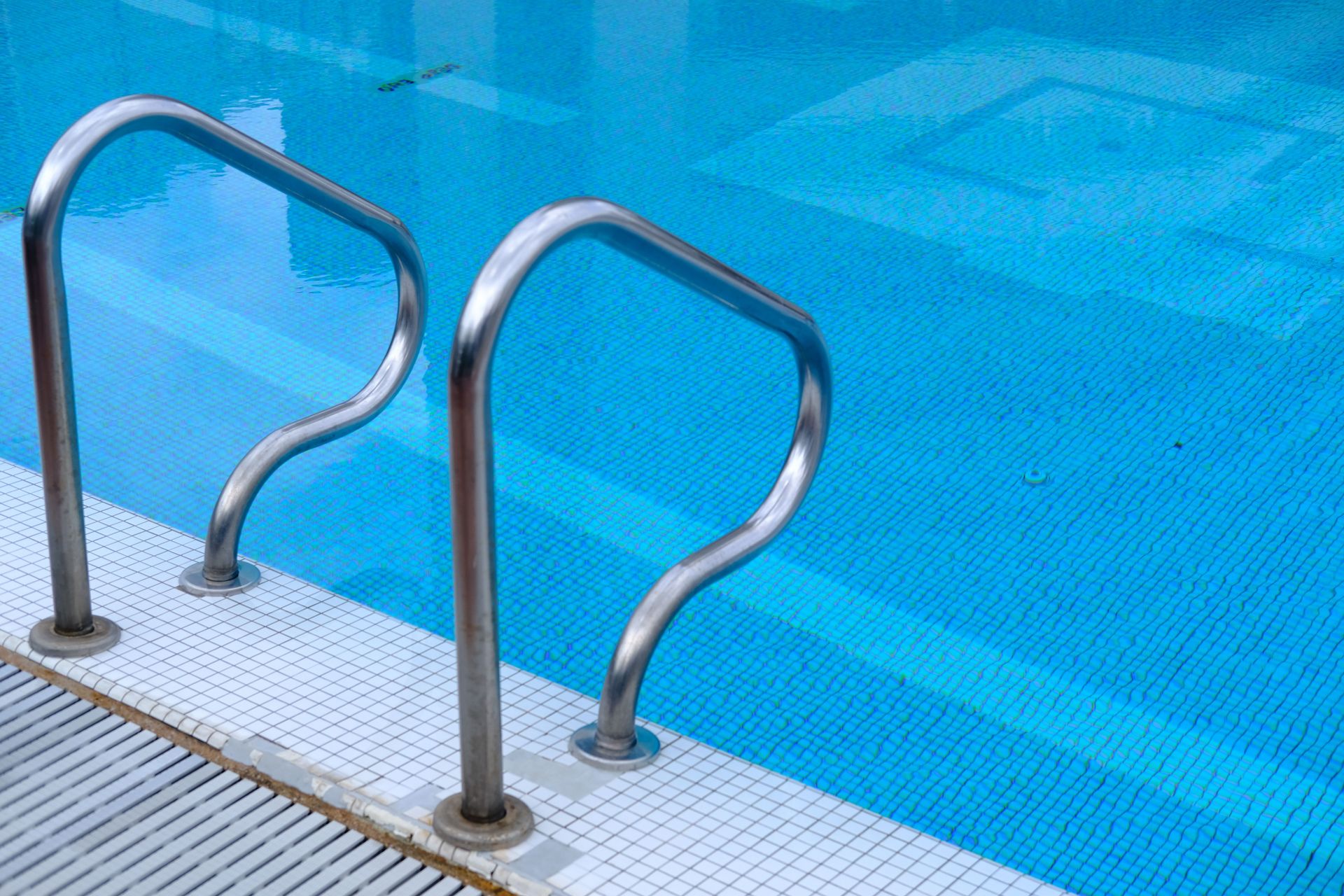 Stainless steel pool ladder leading into a clear blue tiled swimming pool.